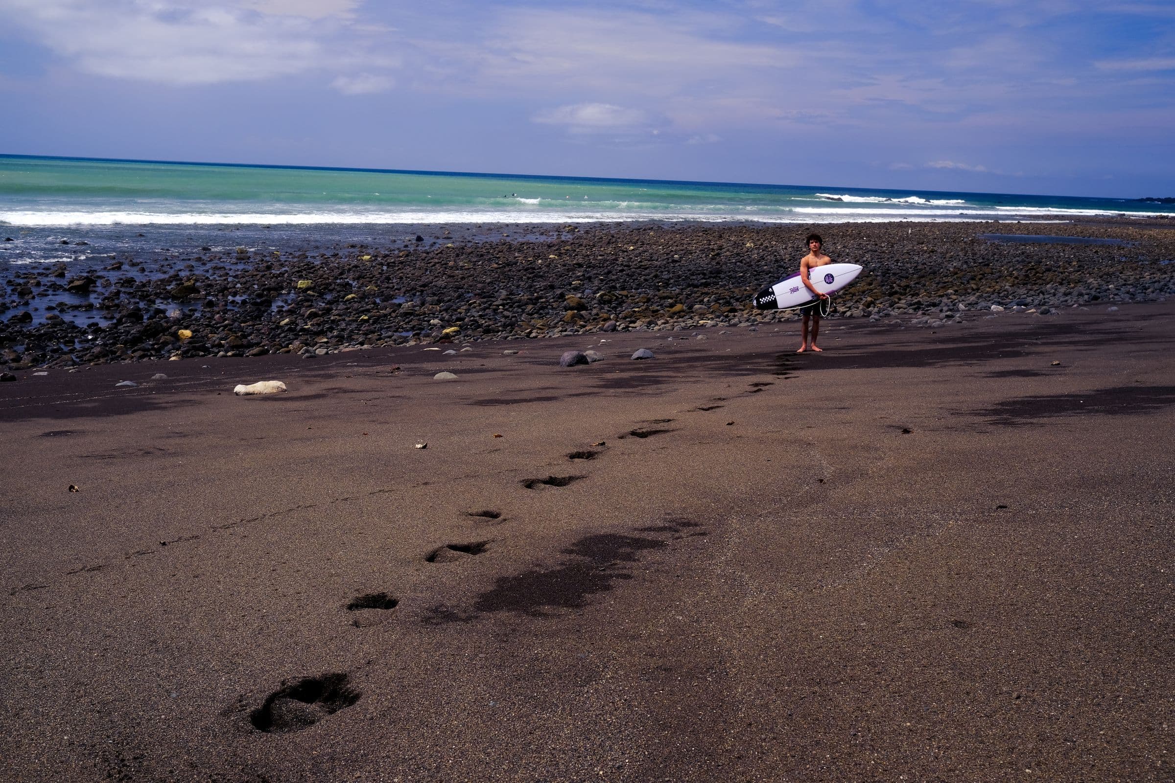 Surfer walking a black-sand beach